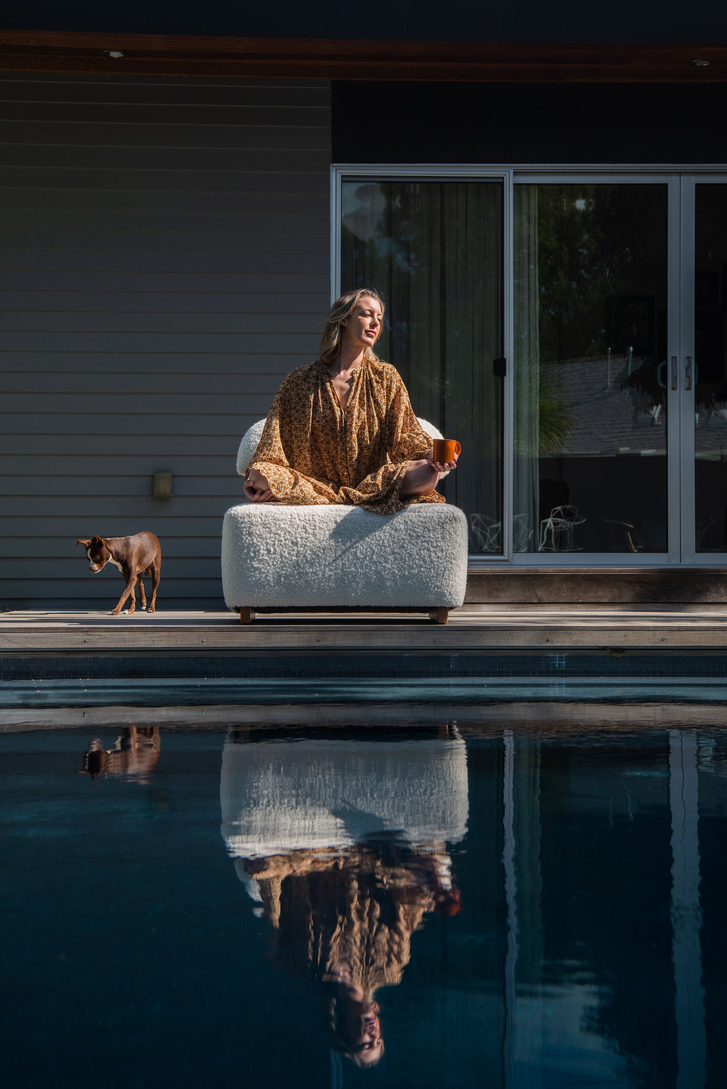 Women Sitting on Meditation Chair by Rue and Williams Home at private residence with a pool and dog standing beside her. Woman is in mediation pose. Modern design with no arms and a curved back, perfect for enhancing mindfulness practices and adding tranquility to any space.